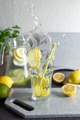 Dynamic water splash of lemon slices dropping into glass. Stone cutting board on kitchen counter....