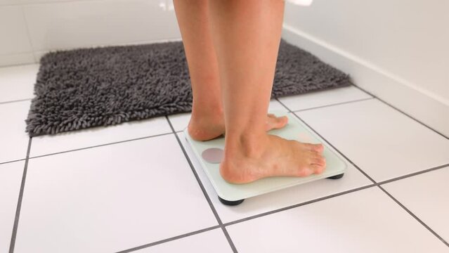 Woman checking her weight by stepping onto a bathroom scale.