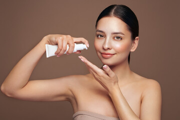Beautiful woman with bottle of moisturizer cream. Video of woman with perfect skin on beige background. Beauty and Skin care concept