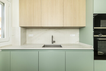 Front image of modern design open kitchen with pastel furniture, white circular decorative hood, columns of integrated appliances