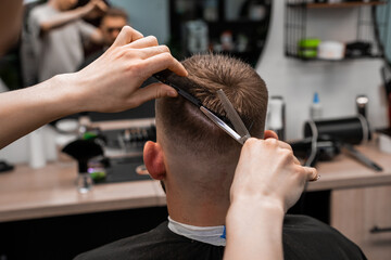 Barber using scissors and comb styling man hair at the barbershop