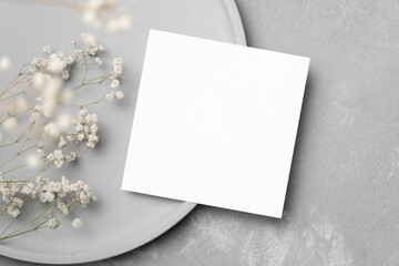 Blank square card mockup with dry gypsophila flower and copy space on grey stylish concrete background, top view