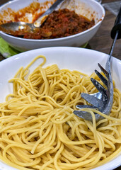 A bowl of spaghetti in the foreground and a bowl of sauce in the background