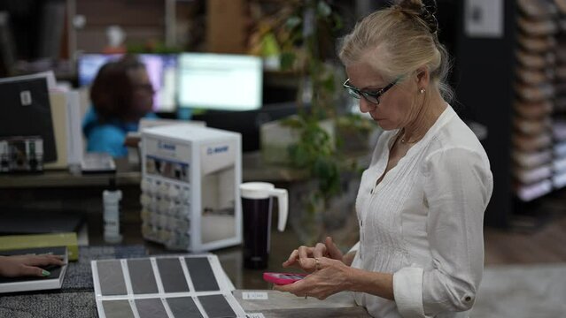 Closeup of mature woman using smart phone in a flooring store calculating cost for home redecorating renovation project.