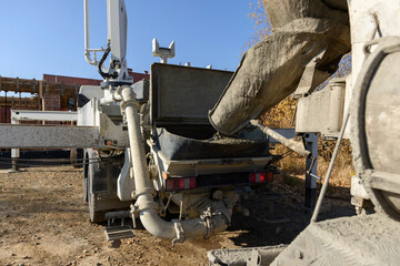 Fototapeta premium Pouring concrete at a construction site. The concrete is poured into the loading hopper of the concrete pump from the concrete mixer guide chute. The process of pouring the foundation in a building.
