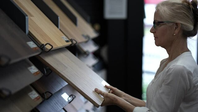 Closeup of happy mature woman running hand across solid or engineered wood plank samples in a floor or hardware store for a home remodeling renovation redecorating project.