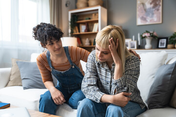 Young lesbian couple having relationship difficulties and arguing at home. Two women sitting on sofa, not talking after argue, feeling depressed and insulted, not talking.