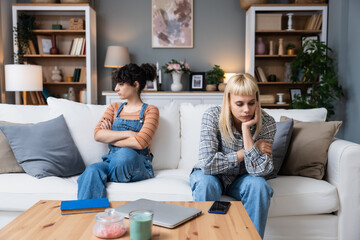 Young lesbian couple having relationship difficulties and arguing at home. Two women sitting on...