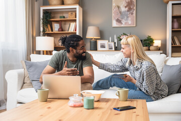 Simple living. Young couple man and woman at home working on laptop, reading book, talking and...