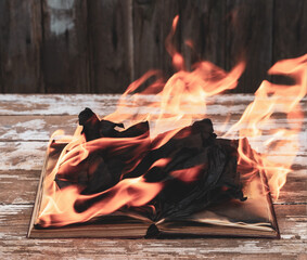 An open book burning in a flame on an old wooden table in closeup