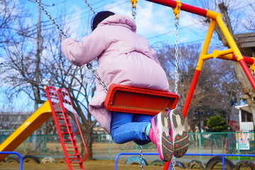 寒い日も元気に外遊び。冬の公園でブランコに乗っている女の子の後ろ姿