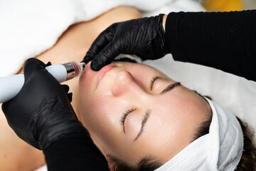 A close-up cosmetologist manipulates a hydropeeling machine to clean and rejuvenate a patient's...