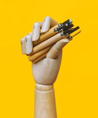A wooden artificial mannequin hand holds a set of linocut cutters on a yellow background. The...