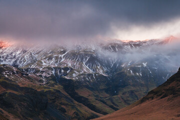 Dramatic view of mist-covered mountains with snow patches in South Iceland