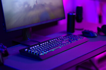 Modern gaming setup with keyboard, mouse, and monitor in a dimly-lit room with purple lighting