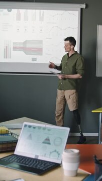 Vertical shot of businessman with lower limb prothesis explaining financial report and giving presentation to team during office meeting