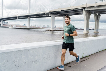 A man jogs along a waterfront path, with a large modern bridge and cityscape visible in the background.