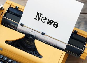 A yellow typewriter with a piece of paper labeled news