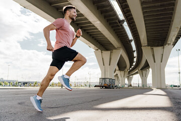 A man runs under a bridge, demonstrating athleticism and speed, with sunlight highlighting his form.