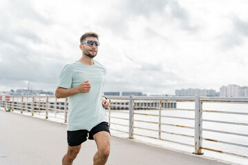 A man in a mint green shirt and black shorts runs by the waterfront under a cloudy sky.