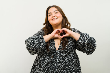 Happy plus-size woman creating a heart shape with her hands against a simple background