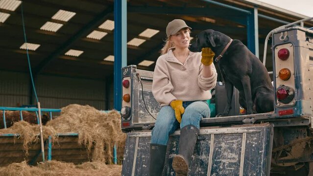 Female farm worker sitting on tailgate of off road farm vehicle with working dog - shot in slow motion