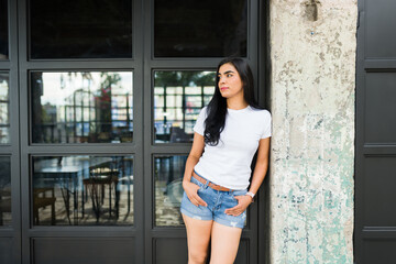 Trendy latin woman posing in a blank white t-shirt mockup, ideal for brand presentation, with an urban backdrop