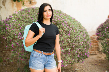 Stylish latin woman in a simple black t-shirt mockup posing in front of lush shrubs, ideal for...