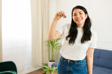 Excited young woman happily poses with new house keys in her sunny living room, beaming with pride...