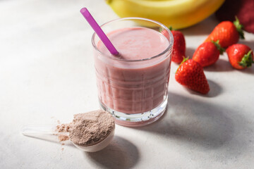 Strawberry and banana smoothie, protein drink in a glass, measuring scoop with whey protein powder,...