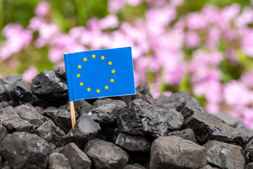 a coal heap with the European Union flag and beautifully blooming flowers in the background. The...