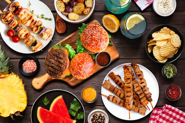 Summer BBQ food table scene. Hamburgers, meat skewers, potatoes, fruit and snacks. Overhead view on...