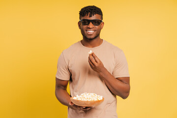 Excited, smiling African American man wearing 3D eyeglasses, eating popcorn, watching movie