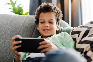 Smiling, attractive African American boy lying holding mobile phone, playing games