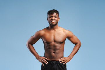 Smiling African American man, athlete with muscular body, naked torso isolated on blue background