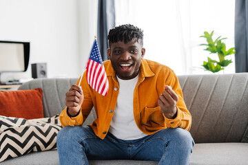 Smiling excited African American man, supporter holding American flag rejoicing, waiting for results