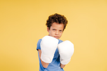 Serious attractive African American little boy boxer wearing white boxing gloves looking at camera