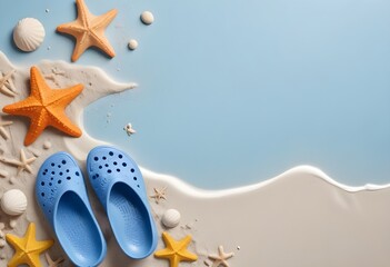  A pair of light blue crocs-style sandals on a sandy beach , with orange starfish decorations on them