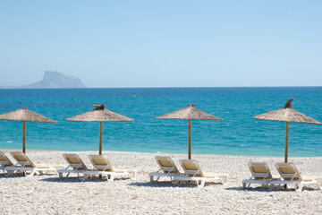 View to turquoise blue Mediterranean Sea and Albir seaside beach in Alicante province, Spain. Raco de Albir Beach with white pebbles, umbrellas and beach sun loungers in beautiful sunny day