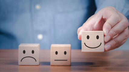 A person is holding wooden blocks with smile face for positive customer satisfaction feedback...