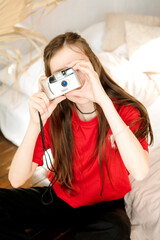 Young woman with long brown hair in a red T-shirt takes pictures with a film camera while sitting...