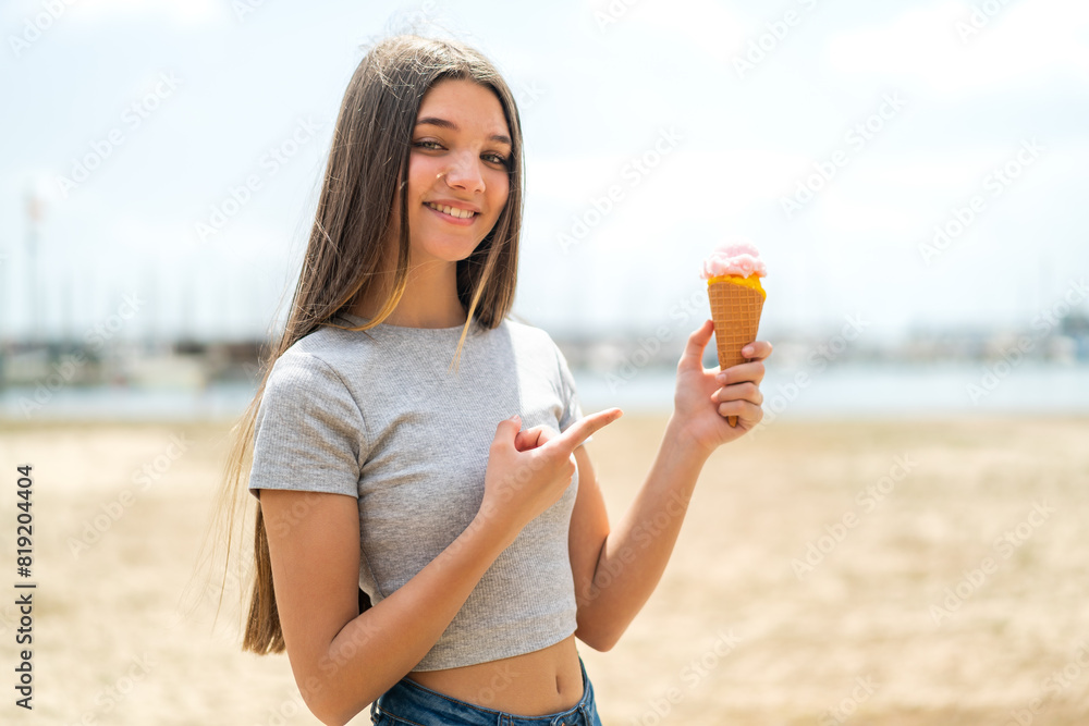 Wall mural Teenager girl with a cornet ice cream at outdoors and pointing it