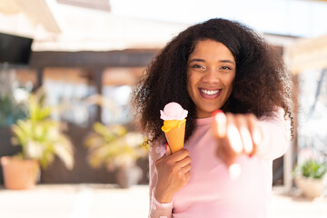 Young African American woman with a cornet ice cream at outdoors points finger at you with a...