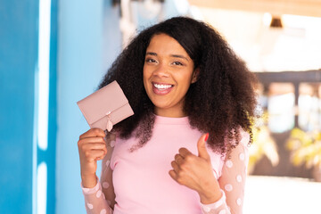 Young African American woman holding a wallet at outdoors with thumbs up because something good has...
