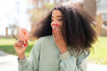 Young African American woman holding a donut at outdoors with surprise and shocked facial expression