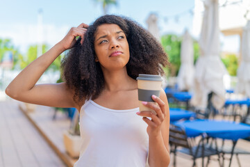 Young African American woman holding a take away coffee at outdoors having doubts and with confuse...