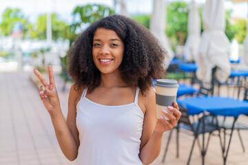 Young African American woman holding a take away coffee at outdoors smiling and showing victory sign