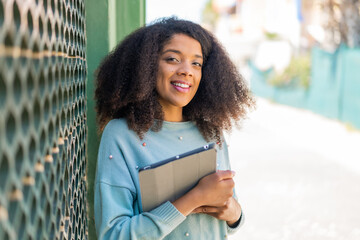 Young African American woman at outdoors holding a tablet with happy expression