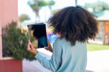 Young African American woman holding a tablet at outdoors in back position