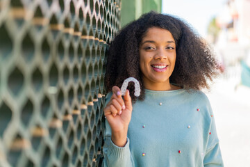 Young African American woman holding invisible braces at outdoors with happy expression